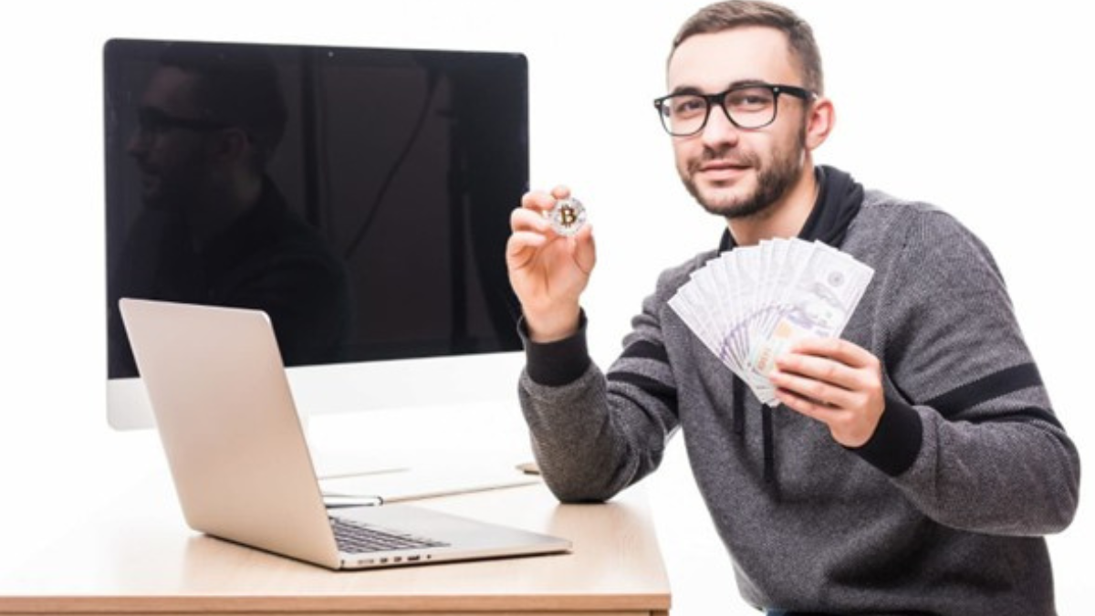 Joven con dinero en efectivo y bitcoin frente a portátil, símbolo de préstamos online rápidos e inversión digital.